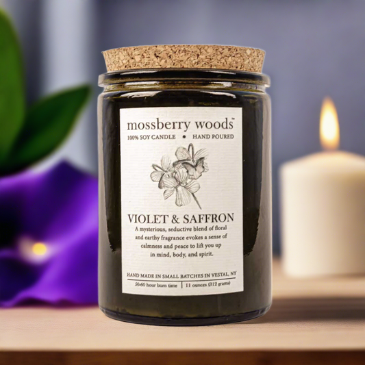 Violet & saffron rustic candle with violet flower and a lit candle in the background