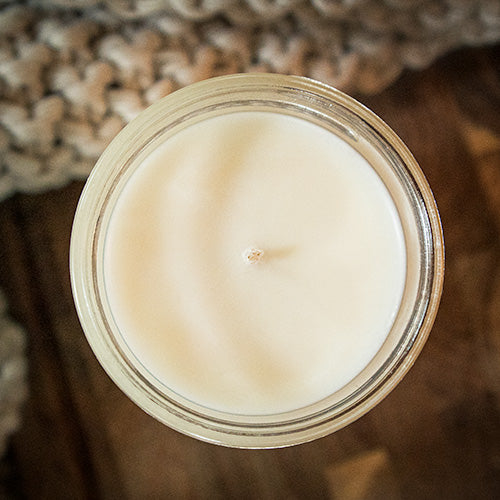 Top view of a Cashmere Cedar Country Cottage soy candle sitting on a wood table with a cozy blanket