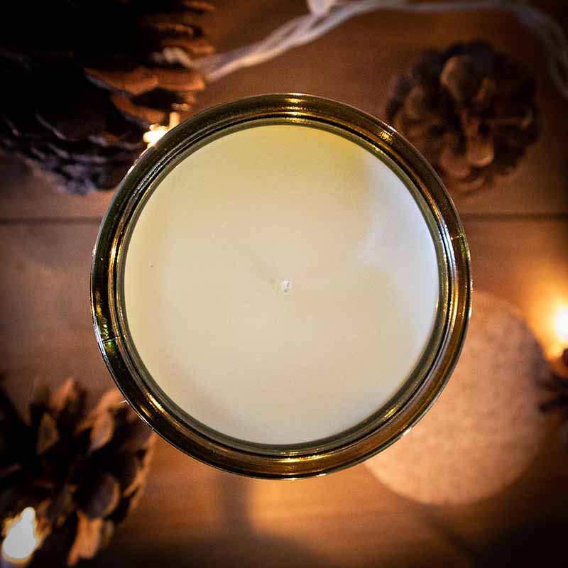 Top view of a candle with pine cones and Christmas lights in the background