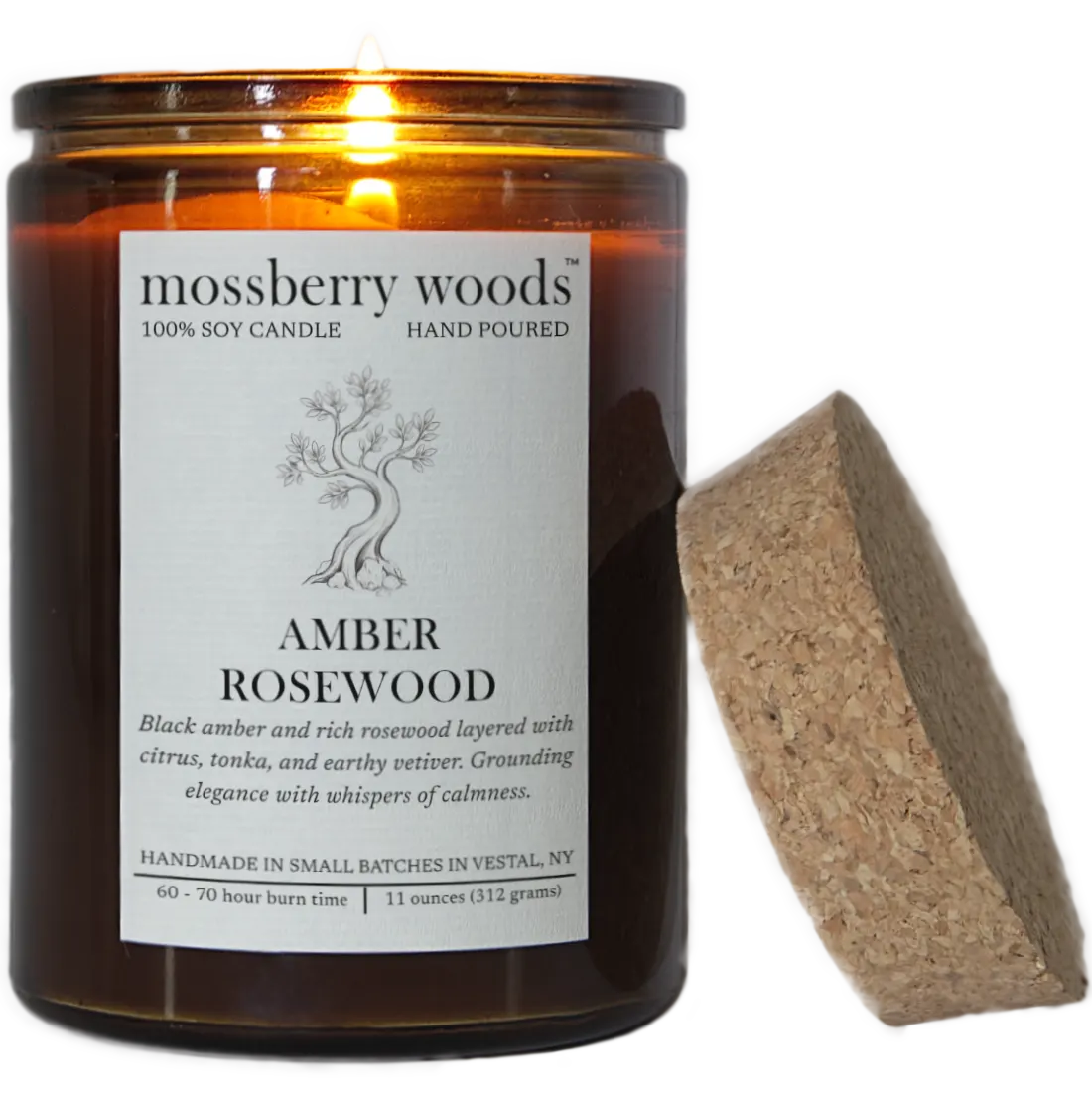 A lit Amber Rosewood scented candle with it's flame illuminating a rustic amber glass container and its cork lid resting on the side. Transparent background.