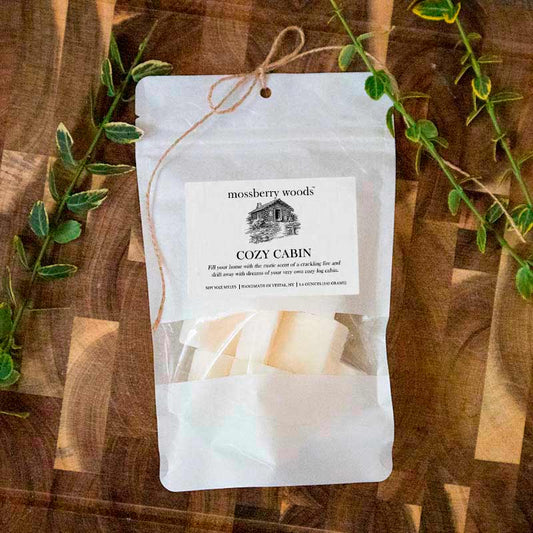 Cozy Cabin scented wax melts in a white bag with a cabin on the label