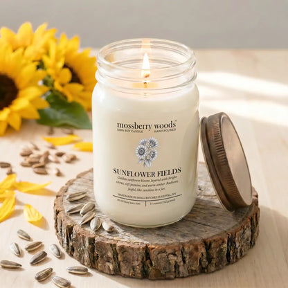 Candle labeled 'Sunflower Fields' by Mossberry Woods on a wooden coaster with sunflowers and seeds.