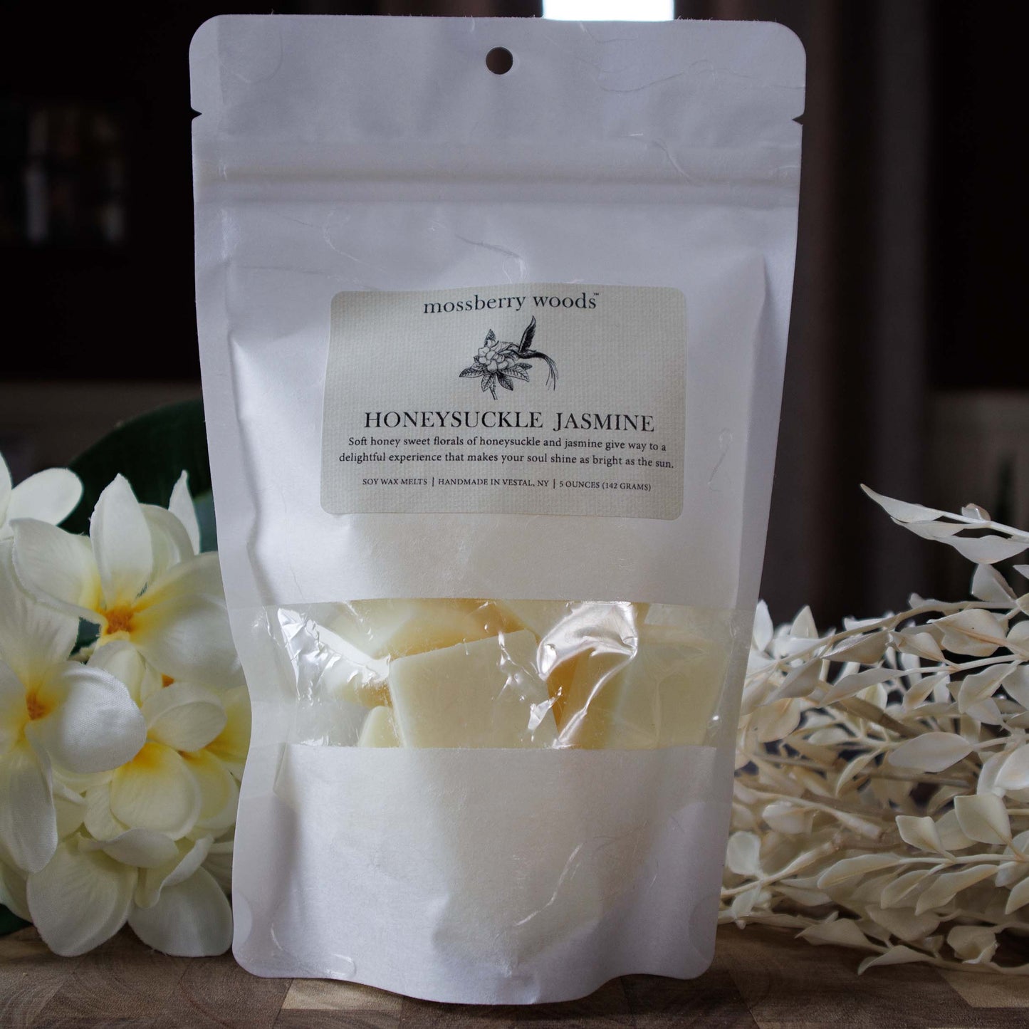 Honeysuckle Jasmine wax melts sitting on a wood table with jasmine flowers in the background