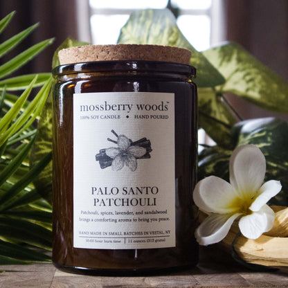 Palo Santo rustic candle in an amber jar against green leaves on a wood table