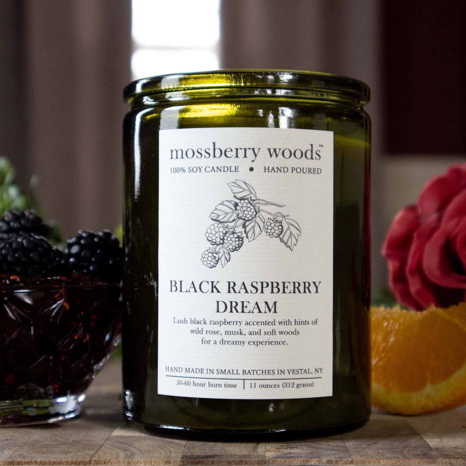 Black Raspberry Dream rustic  candle in a vintage green container with a cork lid sitting on a wooden table with raspberries in a bowl