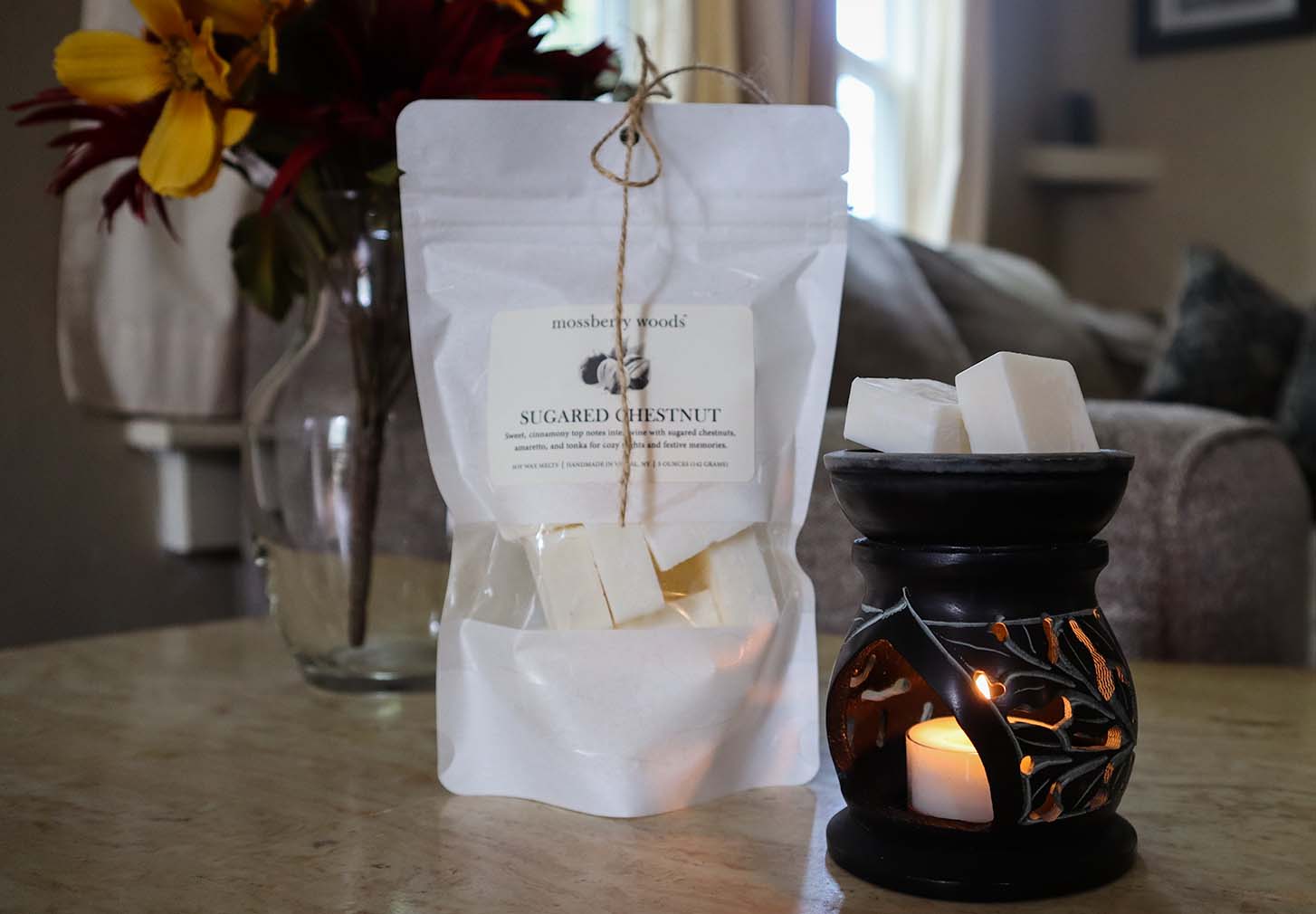 Sugared Chestnut wax melts in a bag on a marble table with a wax melter and flowers in the background